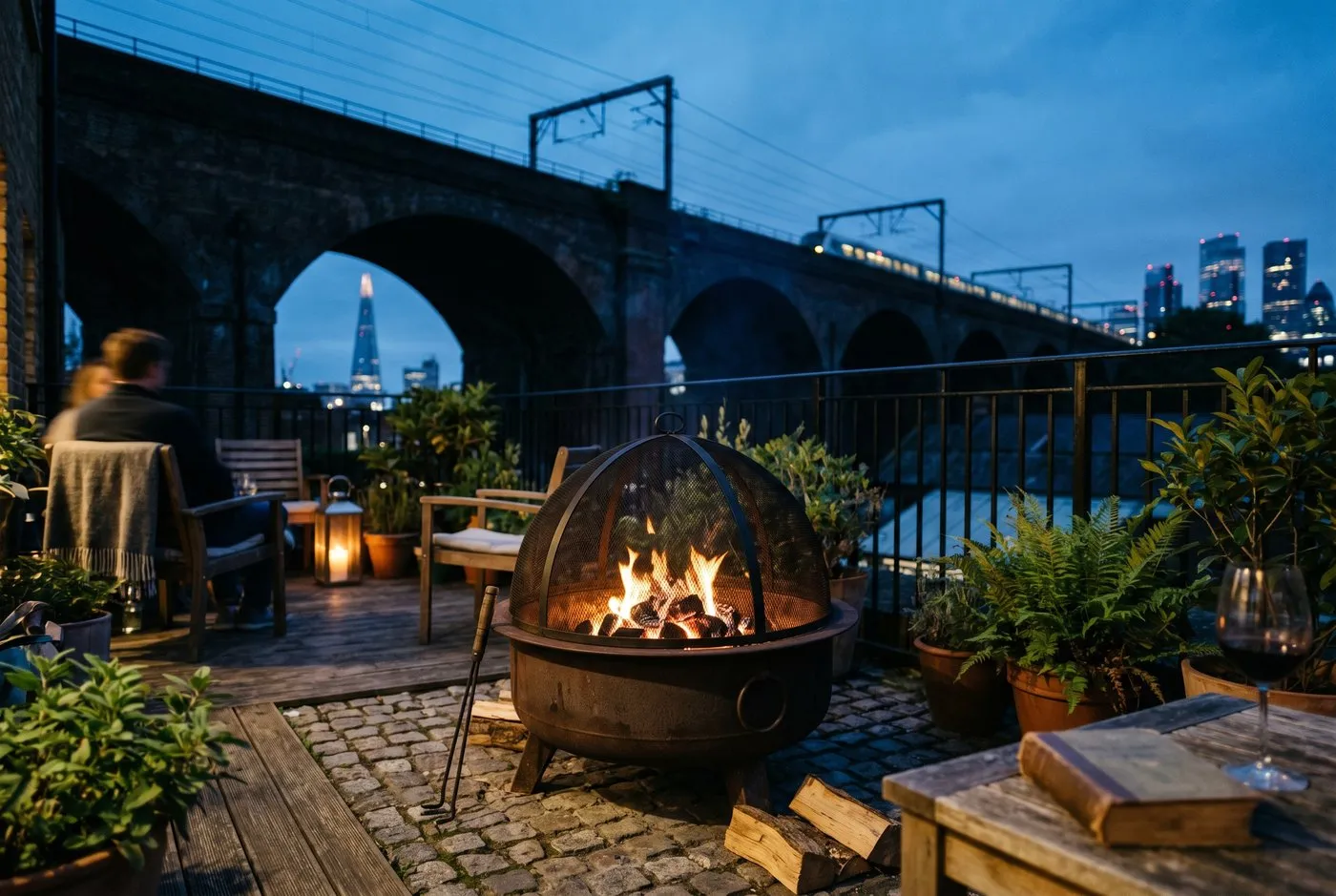 A spark screen mesh dome sitting over a lit fire pit on a UK patio at dusk, catching rising embers to stop ember drift toward nearby planting and fences
