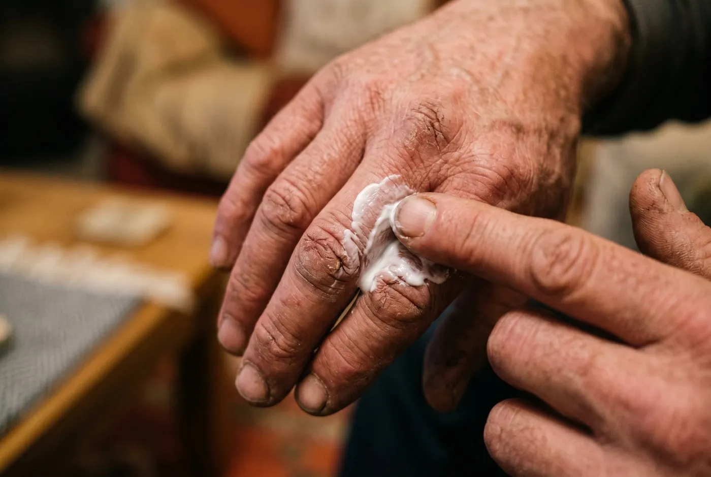 A close-up of thick white repair cream being massaged into the cracked, calloused knuckles of a weathered adult hand