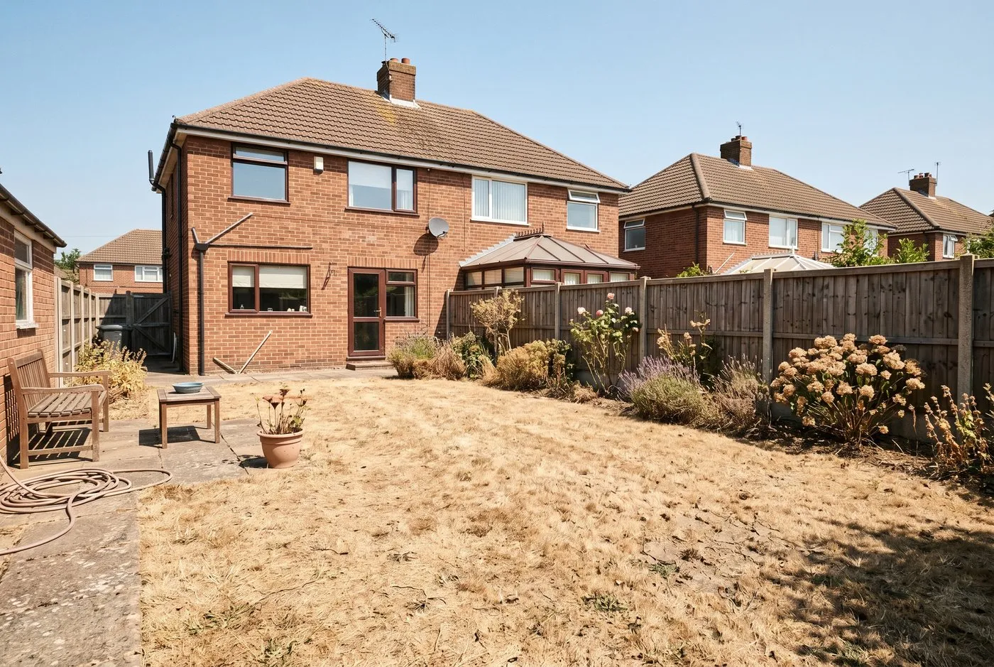 A brown drought-dormant lawn next to a green watered strip in a Scottish garden during a dry summer